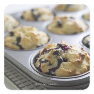 Blueberry muffins in a baking tin on a cooling square sticker