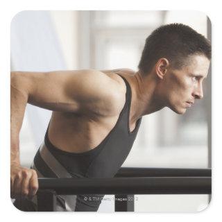 Male athlete using gymnastics equipment in gym square sticker