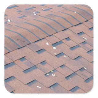 Top view of brown roof shingles with a few fallen square sticker